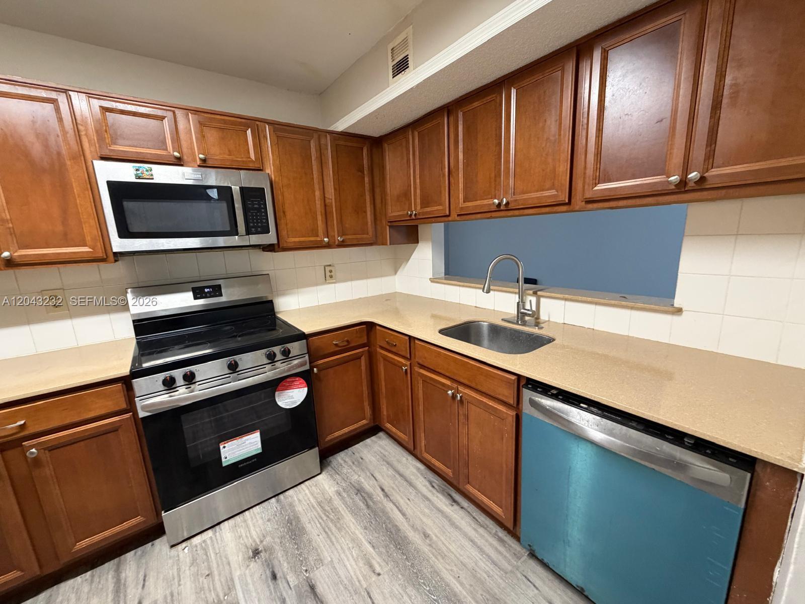 A kitchen features wood cabinets, stainless steel appliances, a beige countertop, and a blue dishwasher — 3400 Foxcroft Rd # 215, Miramar FL 33025, MIRAMAR, FL