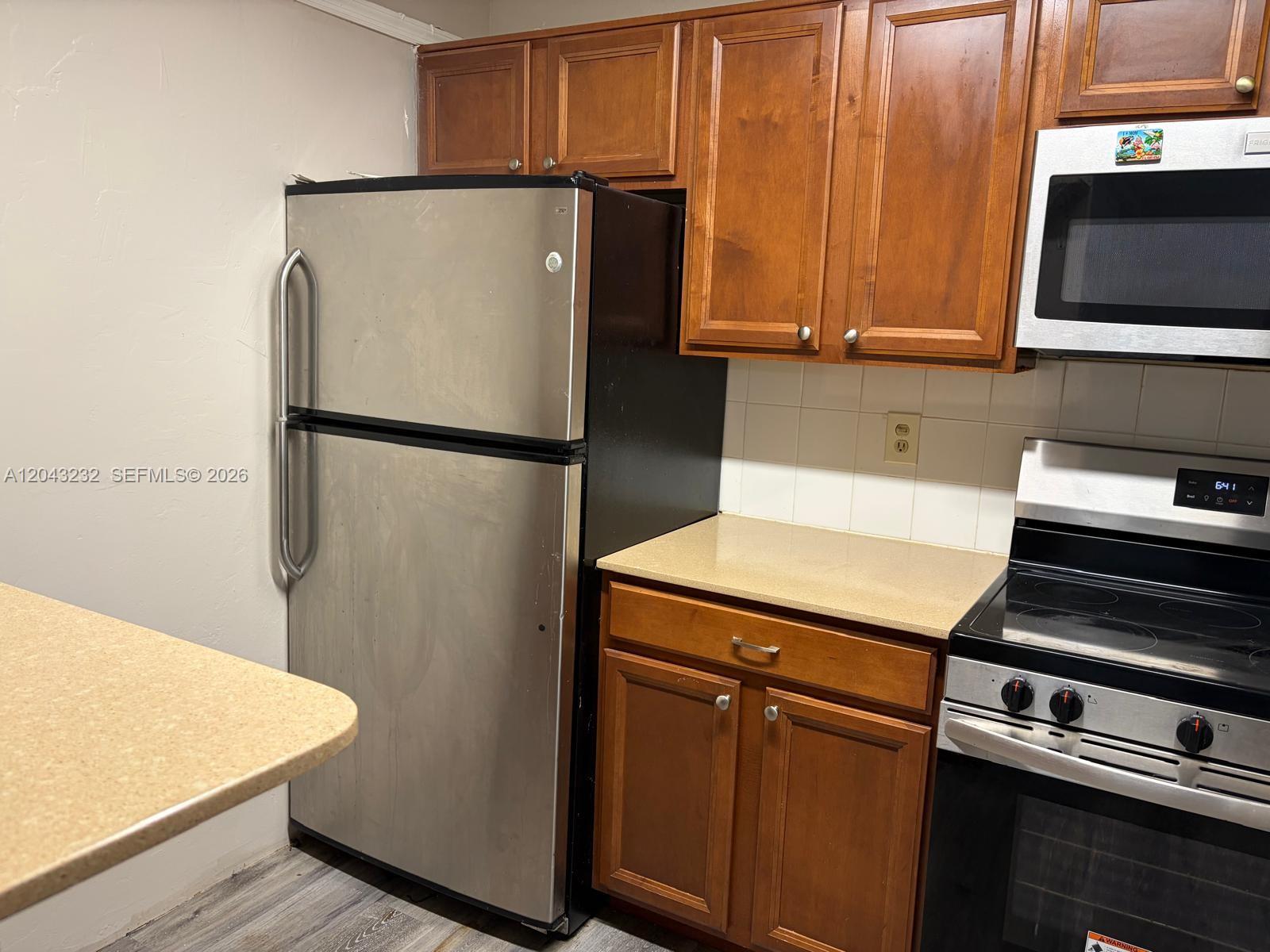 A kitchen features wood cabinets, stainless steel appliances, and beige countertops — 3400 Foxcroft Rd # 215, Miramar FL 33025, MIRAMAR, FL