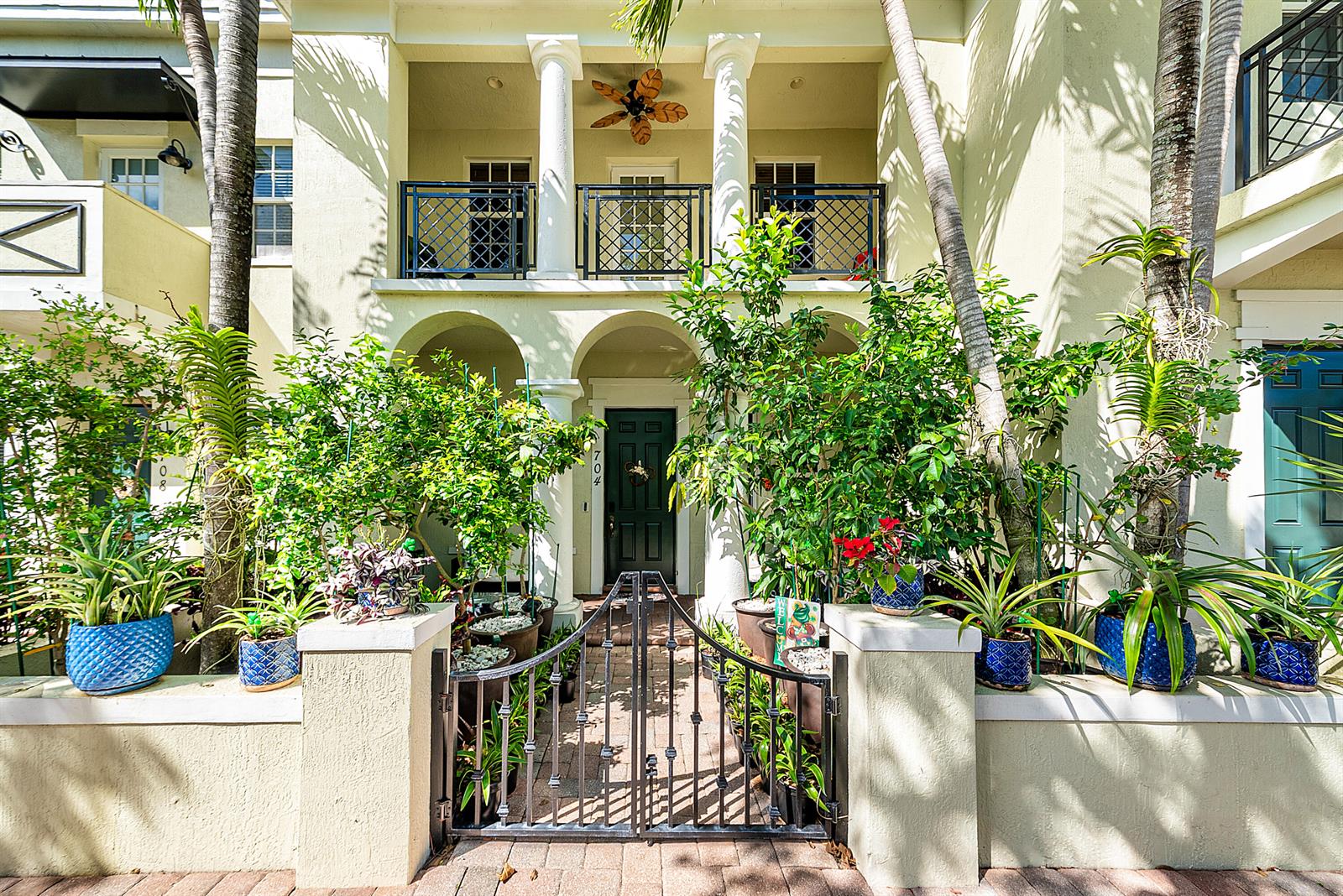 A two-story townhouse exterior features a gated courtyard, white columns, and numerous potted plants — 704 NW 83rd Place, Boca Raton FL 33487, BOCA RATON, FL