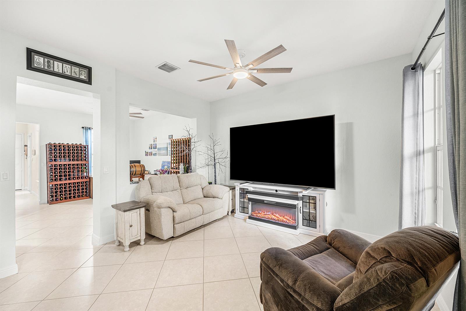 A living room features a large television, an electric fireplace console, and tiled flooring — 704 NW 83rd Place, Boca Raton FL 33487, BOCA RATON, FL