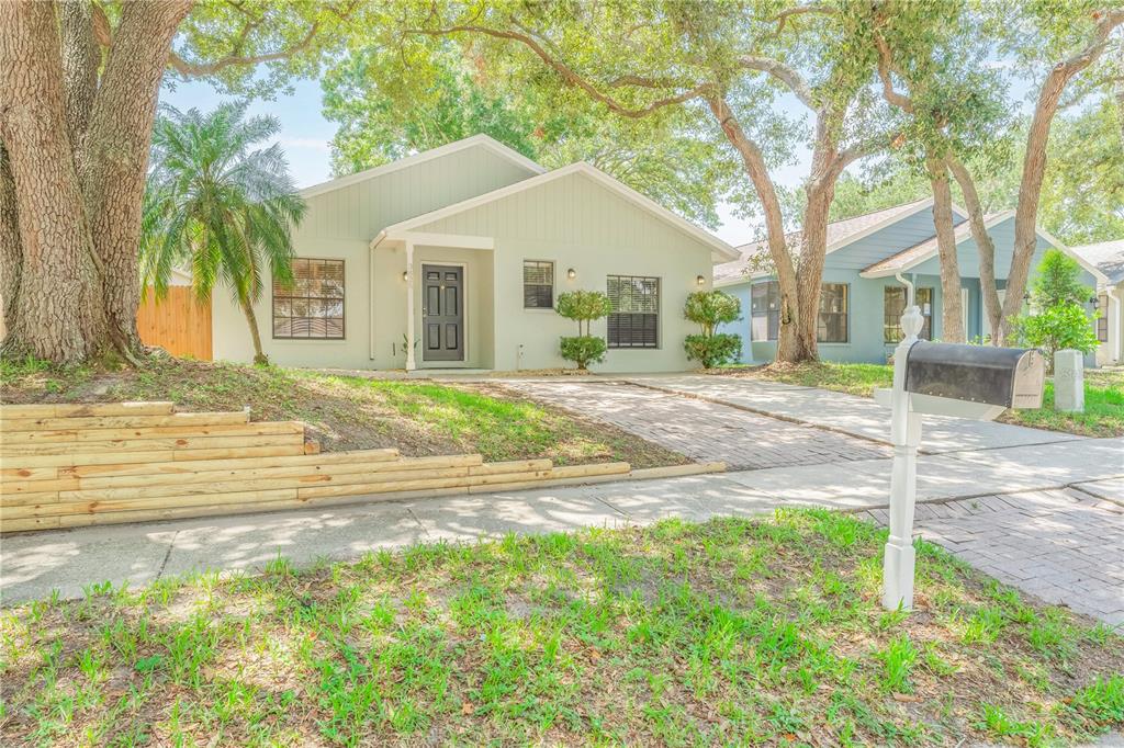 A light green single-story house with a brick driveway, mailbox, and tiered wooden retaining wall — 3826 LAKE SHORE DRIVE, PALM HARBOR, FL