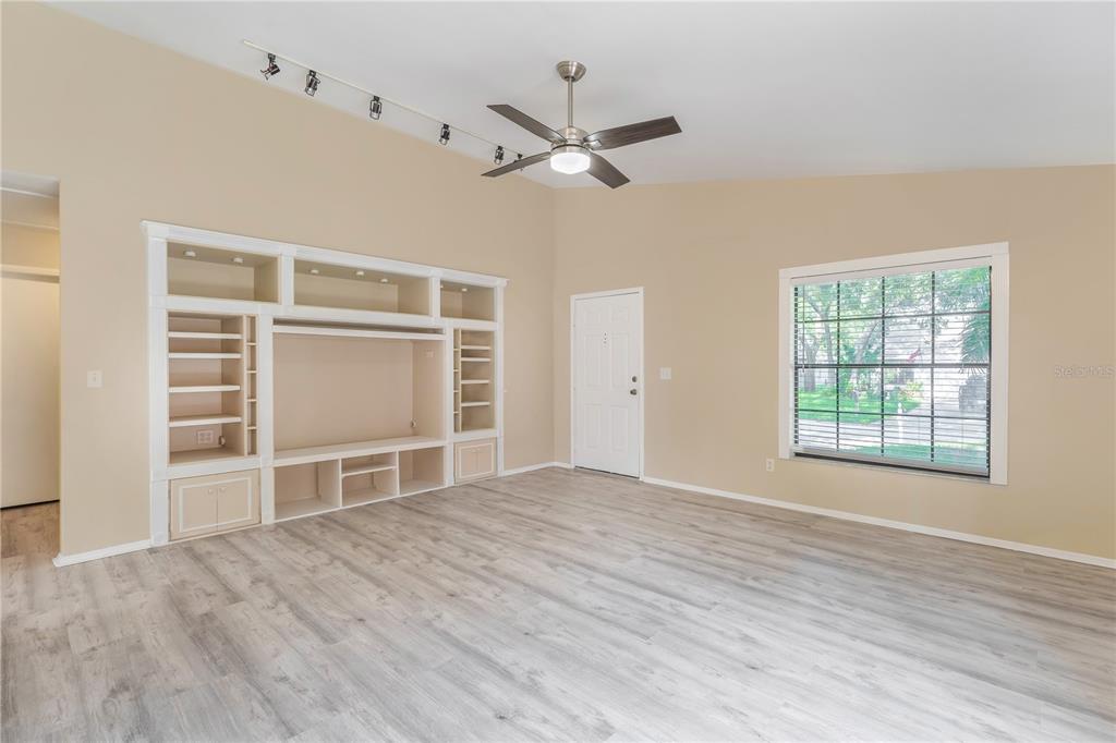 A living room features light wood-look flooring, a large built-in media center, and a ceiling fan — 3826 LAKE SHORE DRIVE, PALM HARBOR, FL