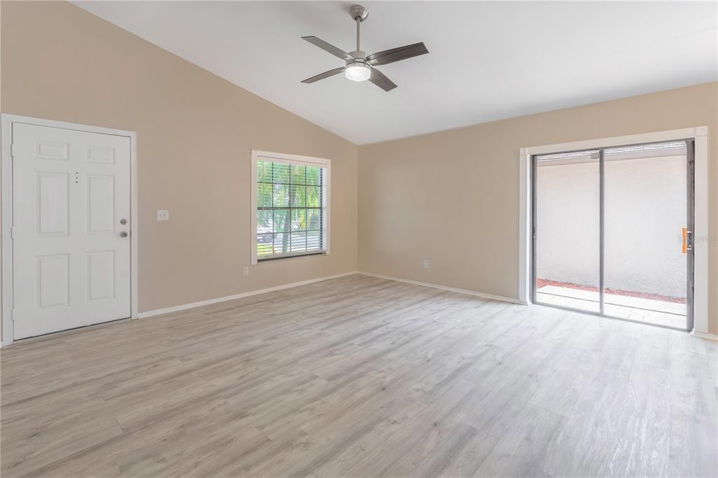 An empty room with light wood-look flooring, a ceiling fan, a window, and sliding doors — 3826 LAKE SHORE DRIVE, PALM HARBOR, FL