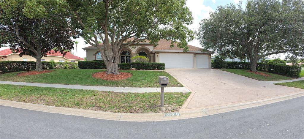 A single-story house with a three-car garage, a paved driveway, and large trees in front — 1028 ARCHWAY DRIVE, SPRING HILL, FL