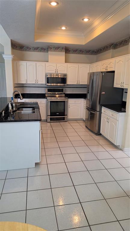 A kitchen features white cabinets, black countertops, stainless steel appliances, and white tiled flooring — 1028 ARCHWAY DRIVE, SPRING HILL, FL