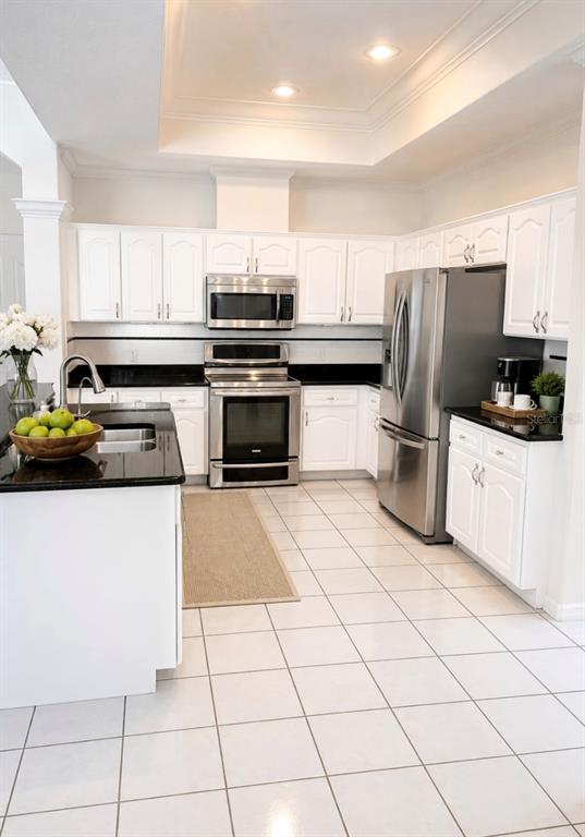 A kitchen features white cabinetry, black countertops, stainless steel appliances, and white tile flooring — 1028 ARCHWAY DRIVE, SPRING HILL, FL