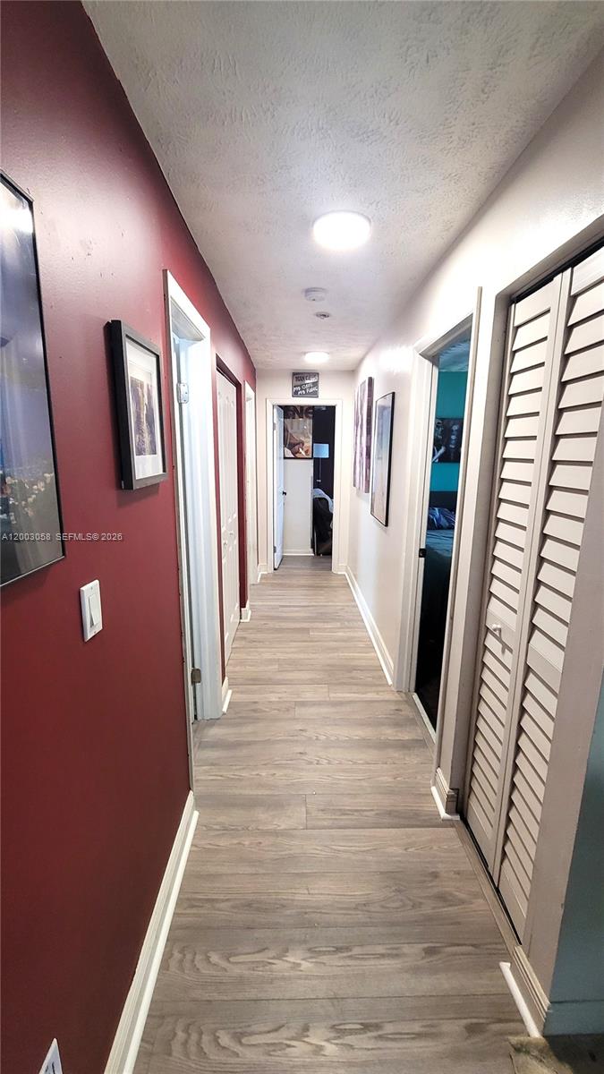 A hallway with wood-look flooring, a red accent wall, and white louvered closet doors — 22113 SW 97th Ct, Cutler Bay FL 33190, CUTLER BAY, FL