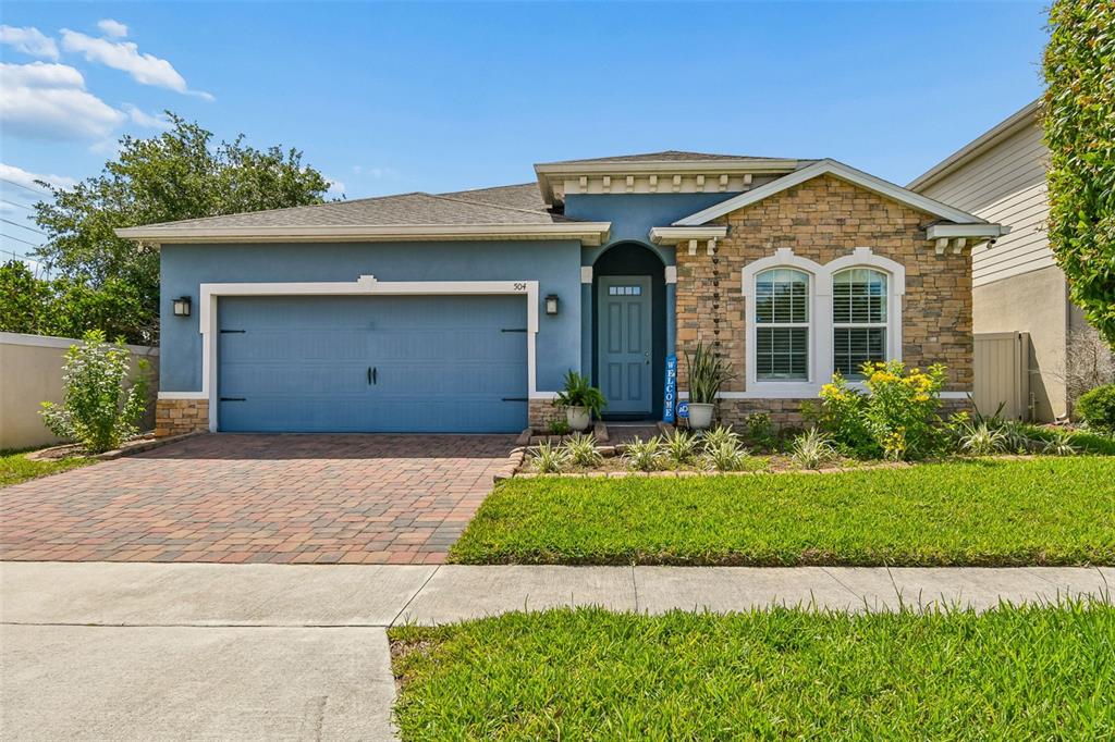 A single-story house with a blue stucco exterior, stone facade, and a paved driveway — 504 AFFIRMED WAY, DAVENPORT, FL