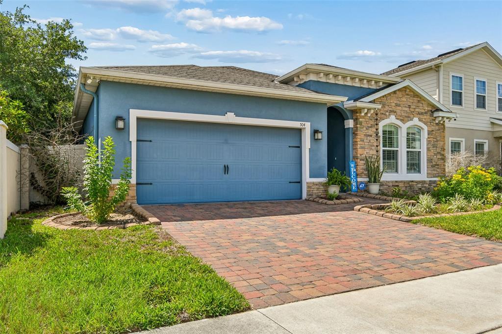 A blue house with a stone facade, a two-car garage, and a brick paver driveway — 504 AFFIRMED WAY, DAVENPORT, FL