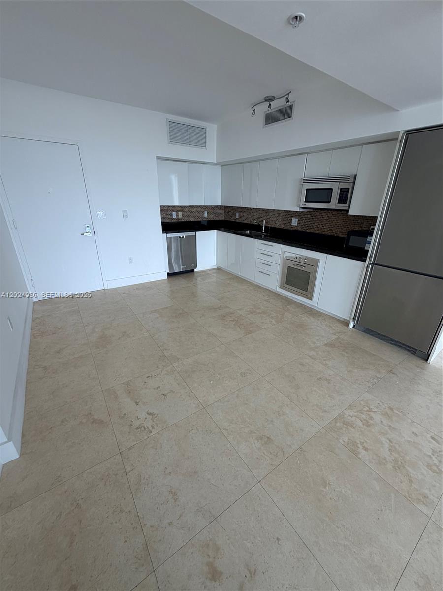 A kitchen features white cabinets, stainless steel appliances, black countertops, and light-colored tile flooring — 92 SW 3rd St # 3909, Miami FL 33130, MIAMI, FL