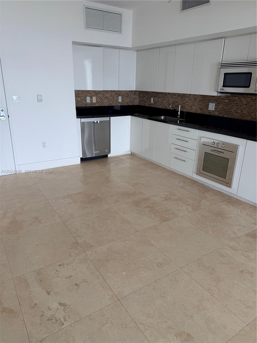 A kitchen features white cabinets, black countertops, a stainless steel dishwasher, and beige tile flooring — 92 SW 3rd St # 3909, Miami FL 33130, MIAMI, FL