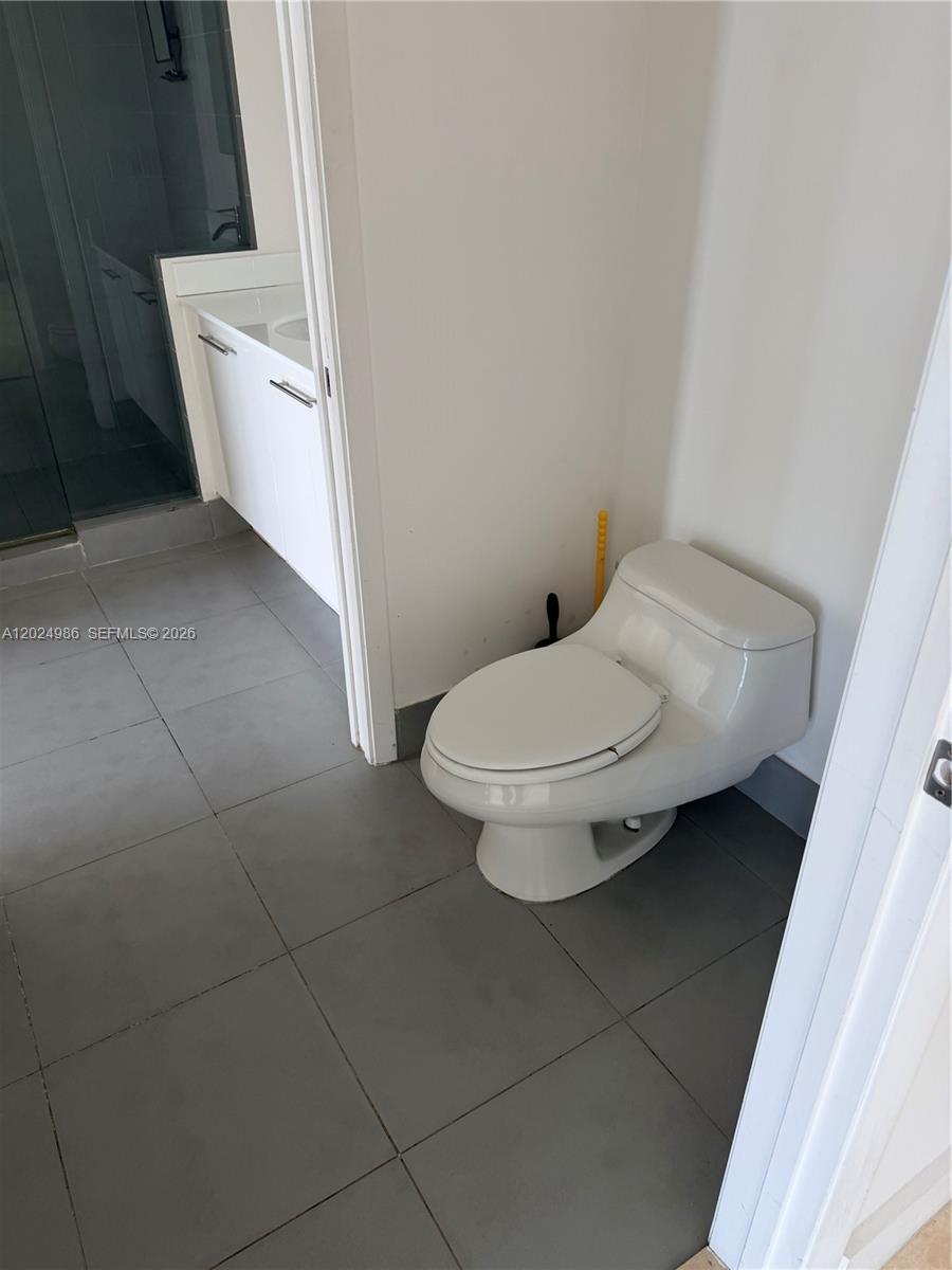 A bathroom features a white toilet on gray tile flooring next to a vanity area — 92 SW 3rd St # 3909, Miami FL 33130, MIAMI, FL