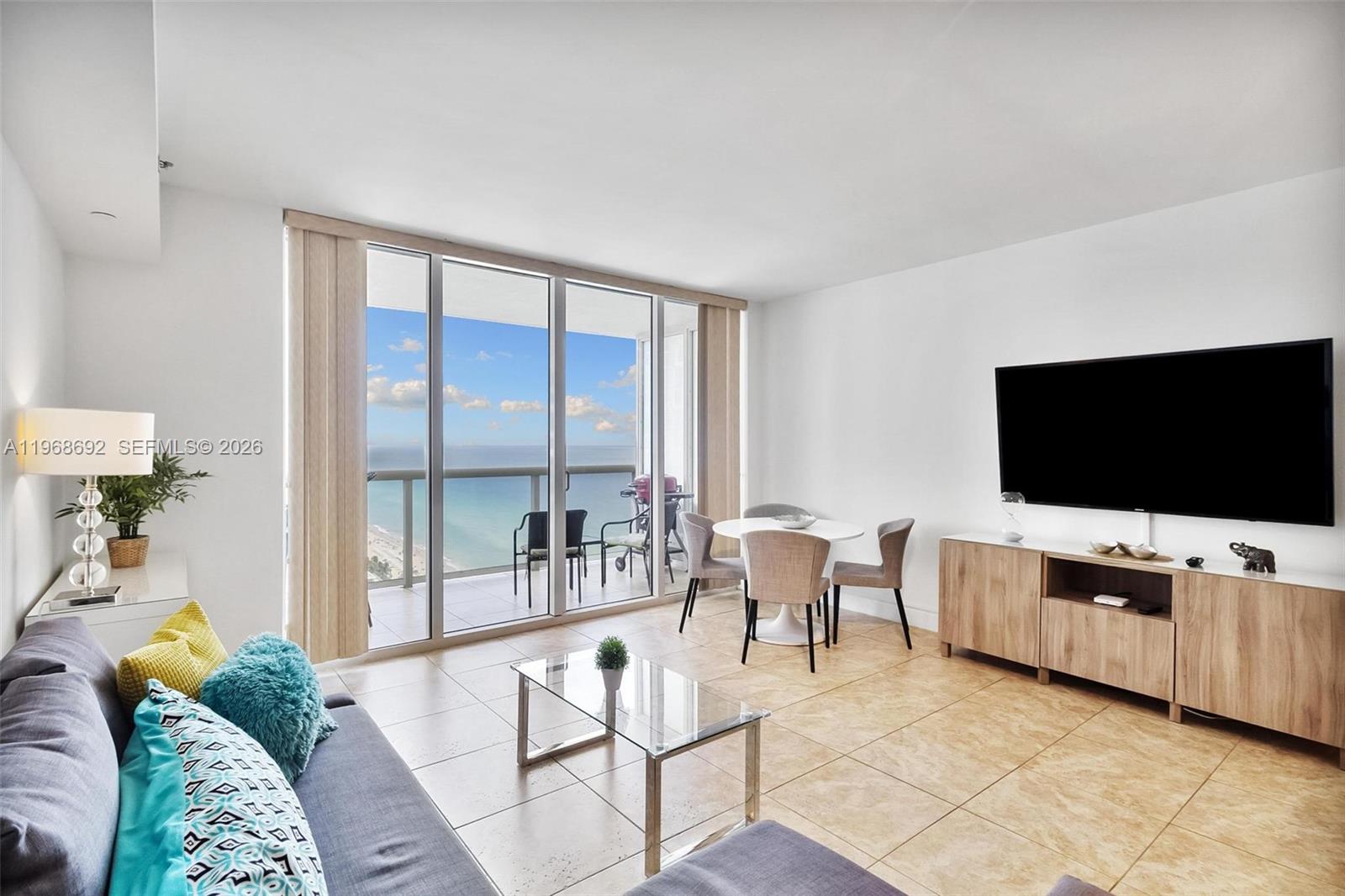 A living room features a glass coffee table, dining area, and balcony with ocean views — 1830 S Ocean Dr # 2409, Hallandale Beach FL 33009, HALLANDALE BEACH, FL