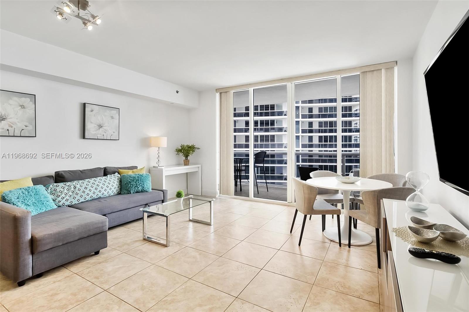 A living and dining area features tile floors, a gray sofa, and a balcony view — 1830 S Ocean Dr # 2409, Hallandale Beach FL 33009, HALLANDALE BEACH, FL