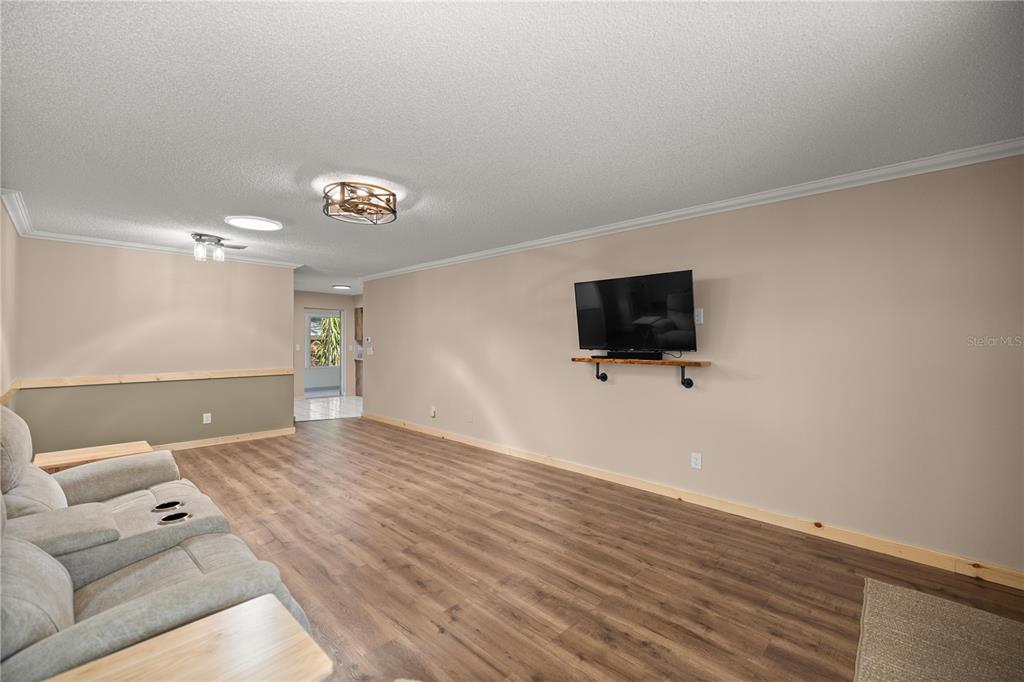 A living room features light-colored walls, wood-look flooring, a wall-mounted television, and a gray sofa — 8637 SW 97TH LANE ROAD UNIT A, OCALA, FL