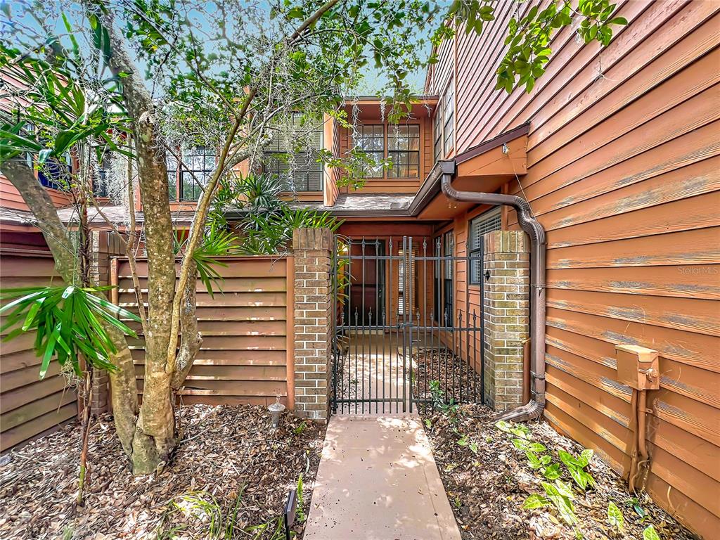 A walkway leads to a gated courtyard entrance of a multi-story wood-sided building — 125 RAINTREE DRIVE, LONGWOOD, FL