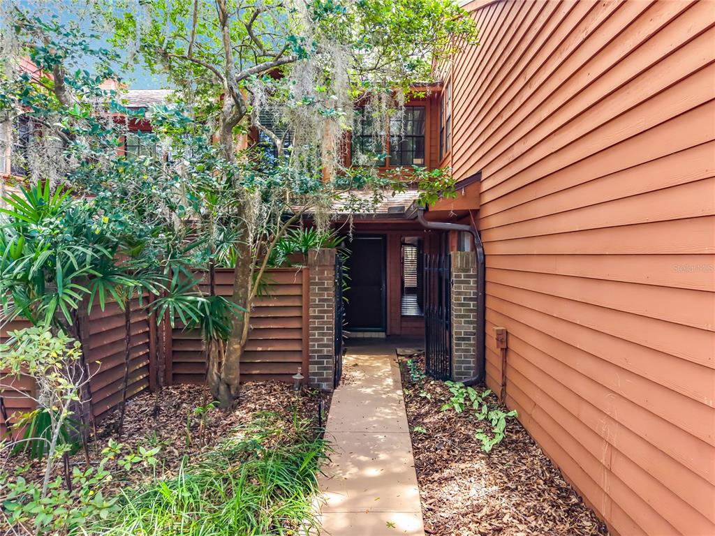 A walkway leads to the front entrance of a house with brown horizontal wood siding — 125 RAINTREE DRIVE, LONGWOOD, FL