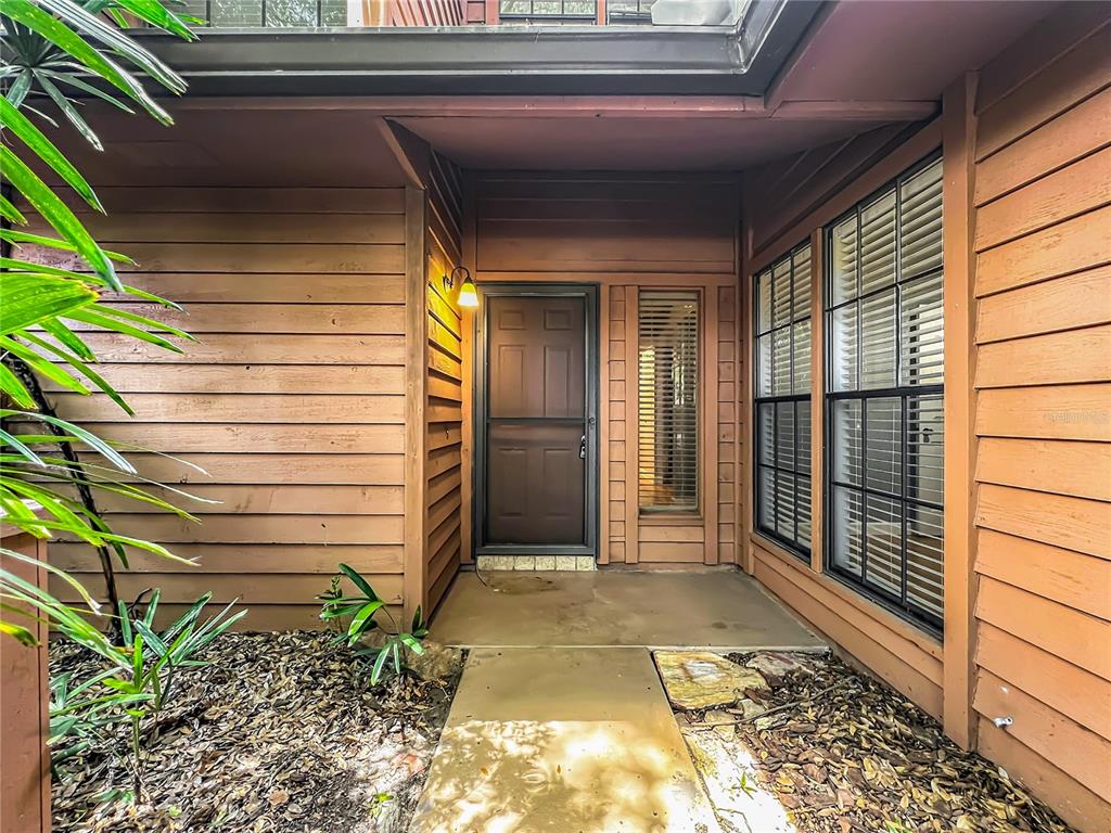 A brown front door with a sidelight is set within a wood-sided home exterior — 125 RAINTREE DRIVE, LONGWOOD, FL