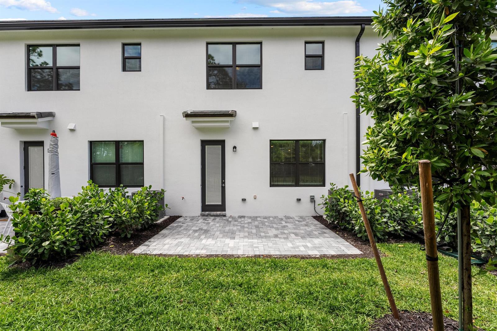 A white townhome exterior features a paved patio, green lawn, and dark-framed windows and doors — 4333 Efendi Drive, Lantana FL 33462, LANTANA, FL