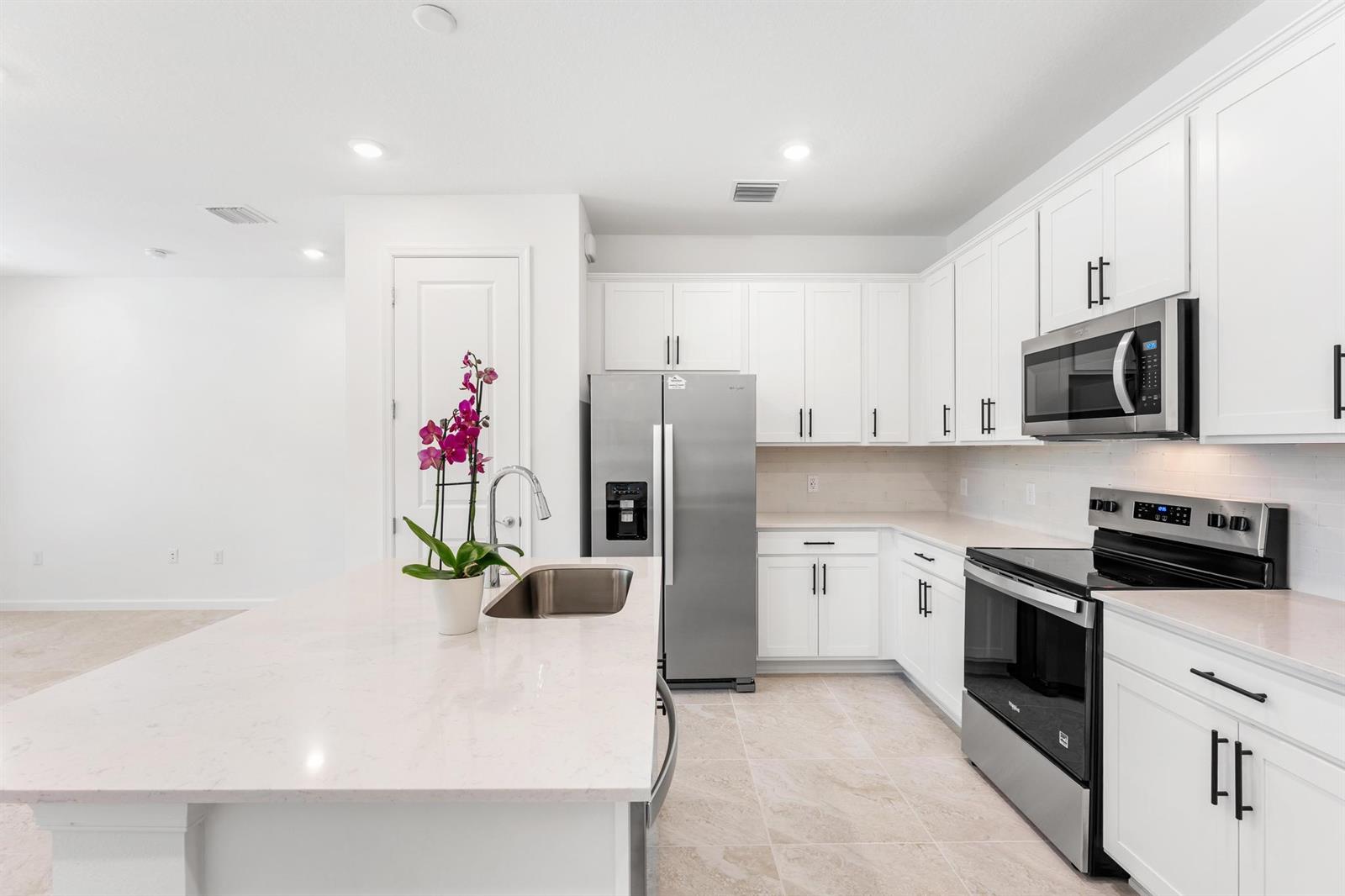 A modern kitchen features white cabinets, stainless steel appliances, and a quartz-topped island with sink — 4333 Efendi Drive, Lantana FL 33462, LANTANA, FL