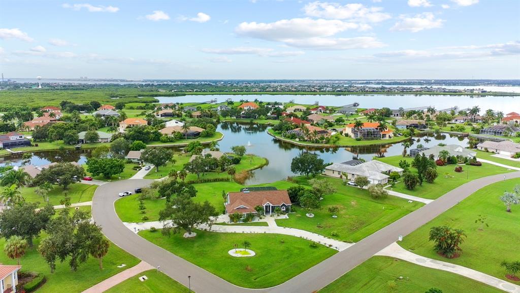 An aerial view shows a suburban neighborhood with houses surrounding a central lake — 6187 9TH AVENUE CIRCLE NE, BRADENTON, FL