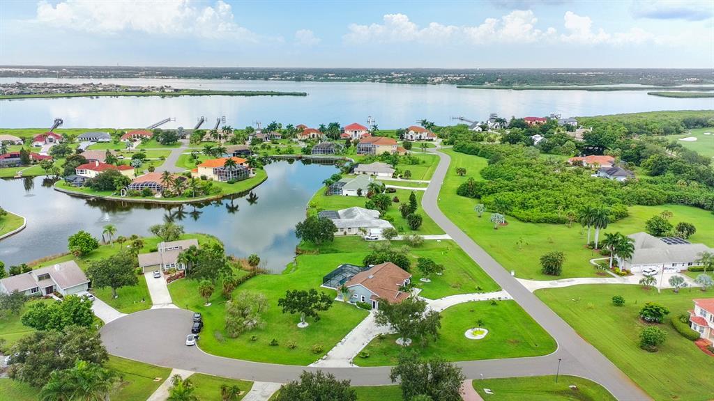 An aerial view of a residential neighborhood featuring houses, a central pond, and a large lake — 6187 9TH AVENUE CIRCLE NE, BRADENTON, FL