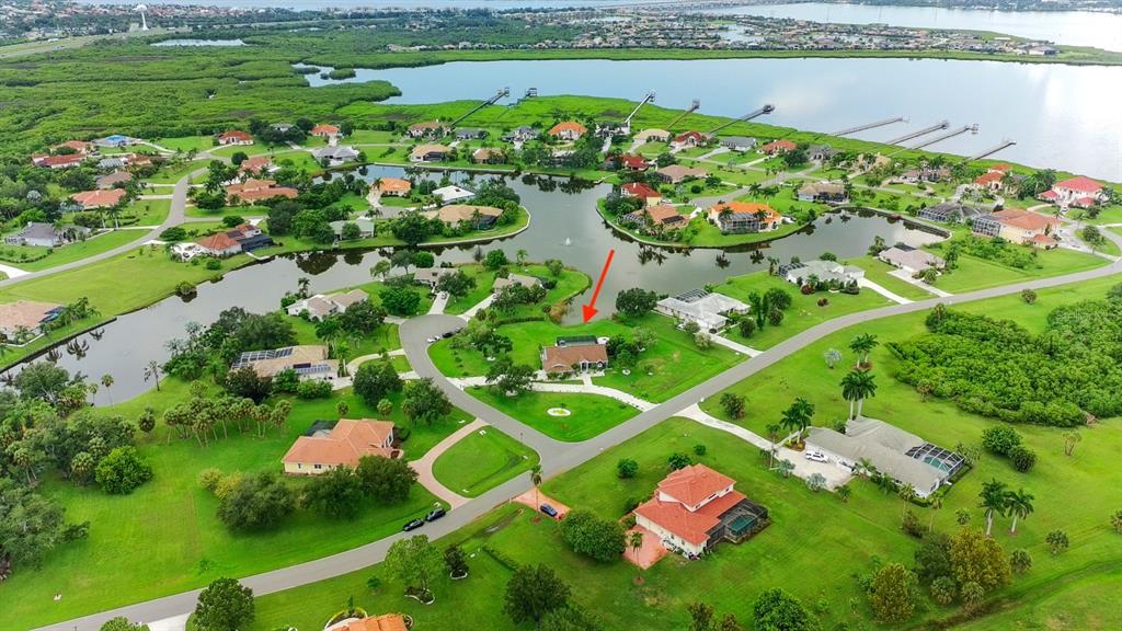 An aerial view of a residential neighborhood featuring houses, green lawns, and a central lake — 6187 9TH AVENUE CIRCLE NE, BRADENTON, FL