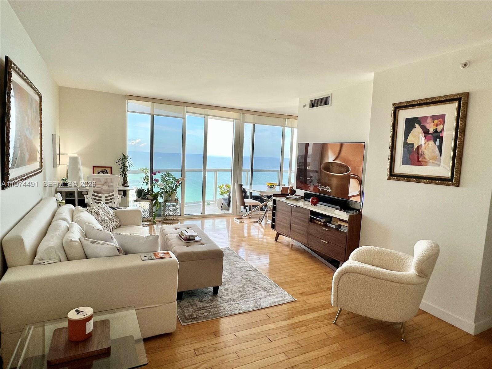 A living room with light wood floors, a white sofa, and floor-to-ceiling windows overlooking the ocean — 6365 Collins Ave # 3609, Miami Beach FL 33141, MIAMI BEACH, FL