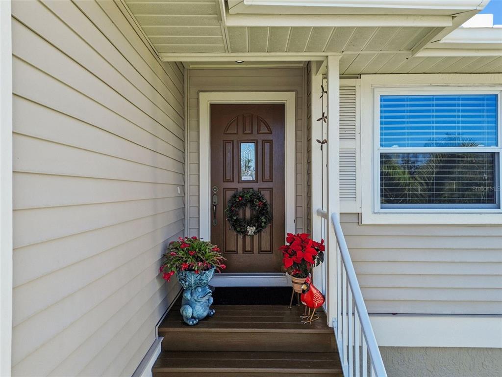 A brown front door with a wreath sits at the top of wooden porch steps — 1059 S POINTE ALEXIS DR, TARPON SPRINGS, FL