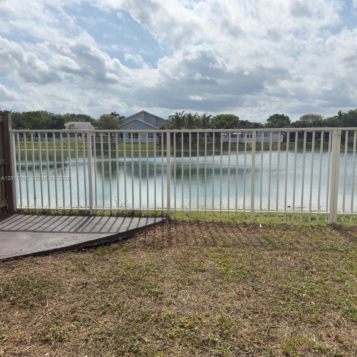 A white metal fence overlooks a lake behind a house with a concrete patio — 148 NE 36 Ave RD, Homestead FL 33033, HOMESTEAD, FL