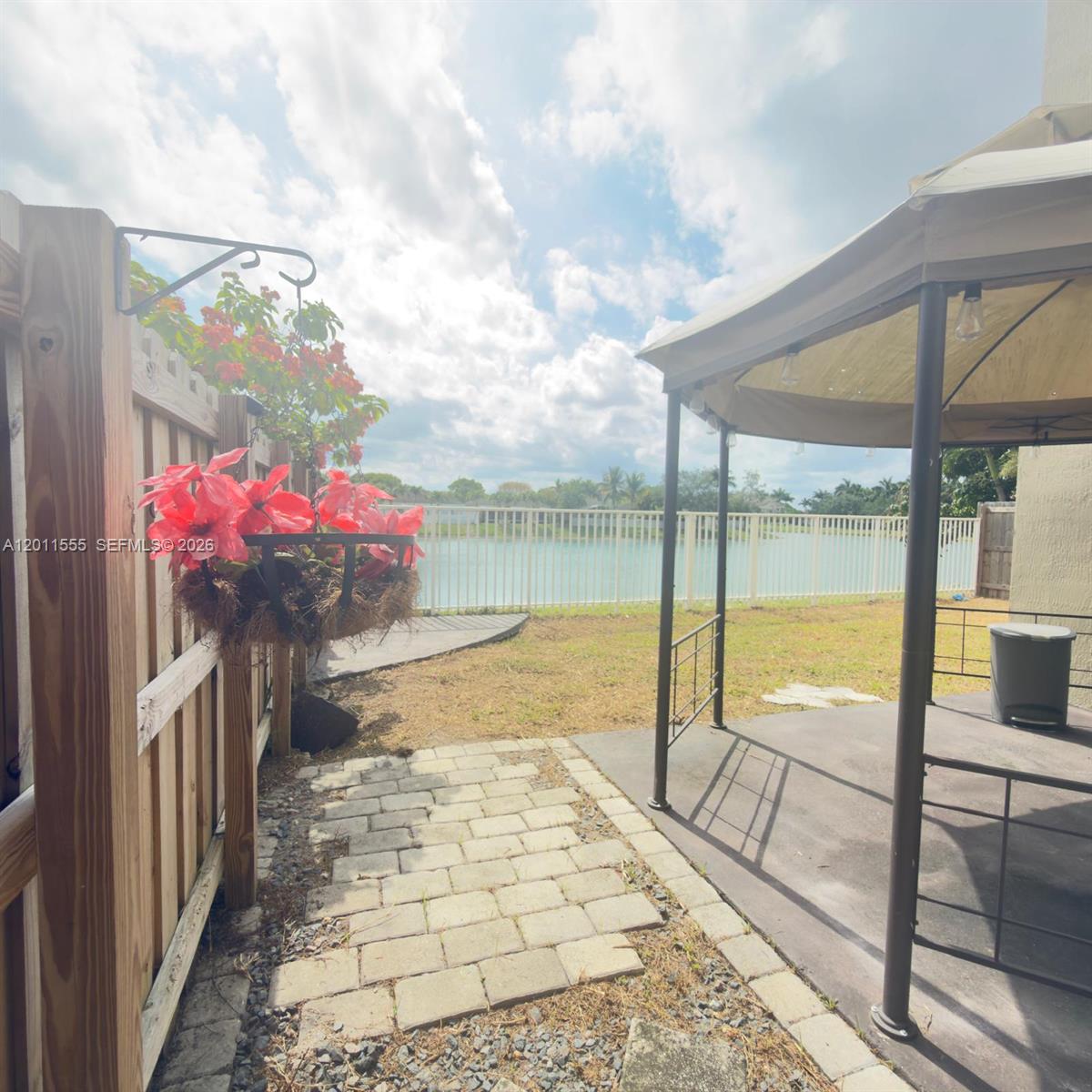 A backyard patio features a gazebo, a hanging flower basket, and a white fence overlooking water — 148 NE 36 Ave RD, Homestead FL 33033, HOMESTEAD, FL
