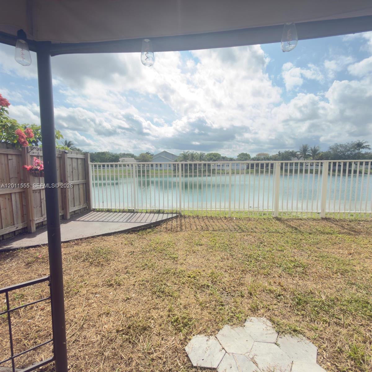 A backyard view features a white fence, a small lake, and a patch of grass — 148 NE 36 Ave RD, Homestead FL 33033, HOMESTEAD, FL