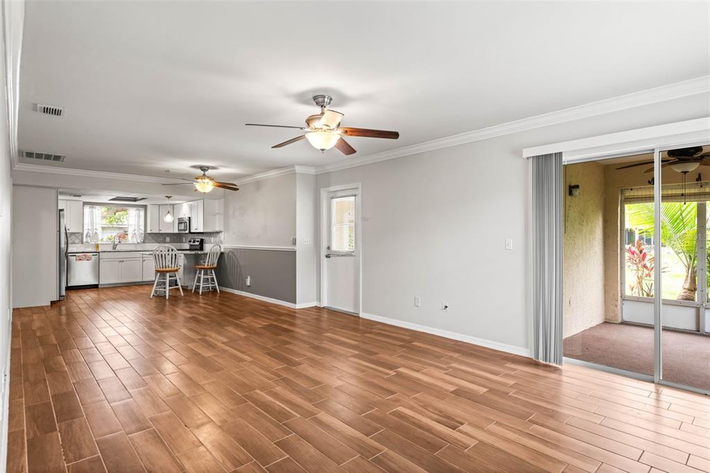An open-concept living area with wood-look tile flooring, a kitchen, and sliding glass patio doors — 2011 HADRIAN COURT UNIT 2011, SUN CITY CENTER, FL