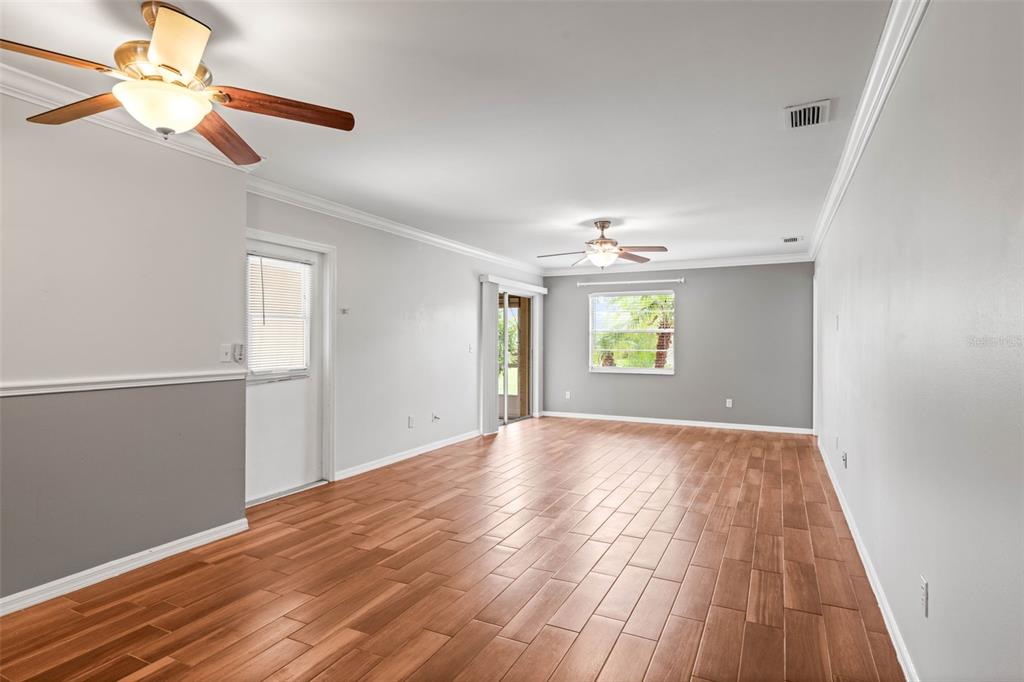 An empty living room features wood-look tile flooring, two ceiling fans, and gray walls — 2011 HADRIAN COURT UNIT 2011, SUN CITY CENTER, FL