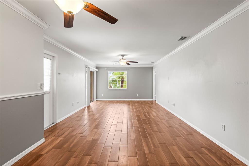 An empty living room features wood-look flooring, white walls with chair rail molding, and ceiling fans — 2011 HADRIAN COURT UNIT 2011, SUN CITY CENTER, FL