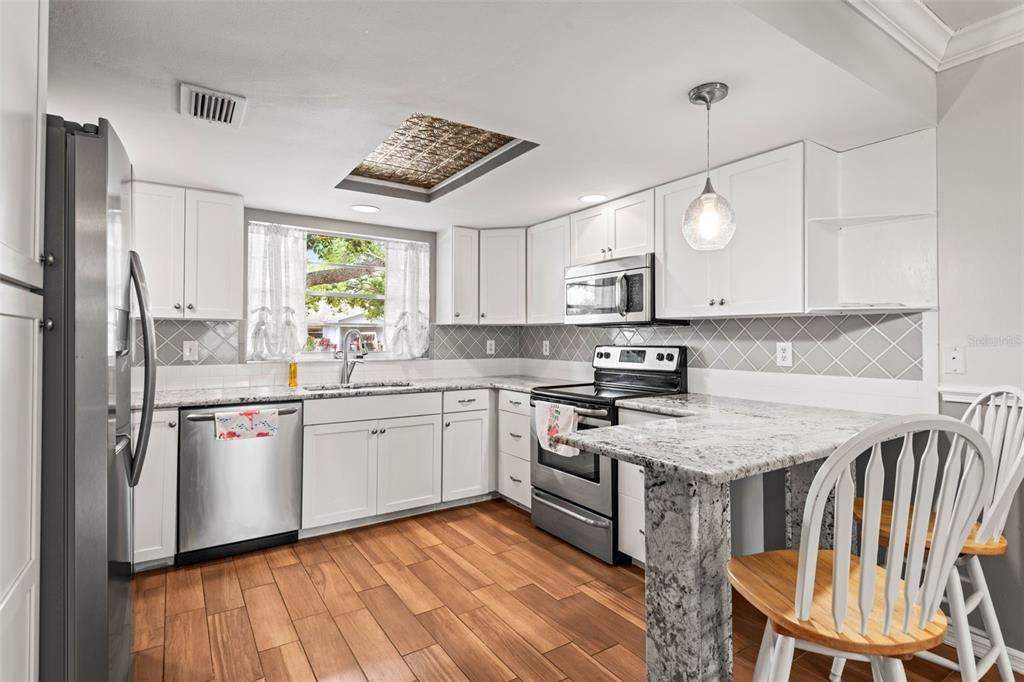 A kitchen features white cabinets, granite countertops, stainless steel appliances, and wood-look tile flooring — 2011 HADRIAN COURT UNIT 2011, SUN CITY CENTER, FL