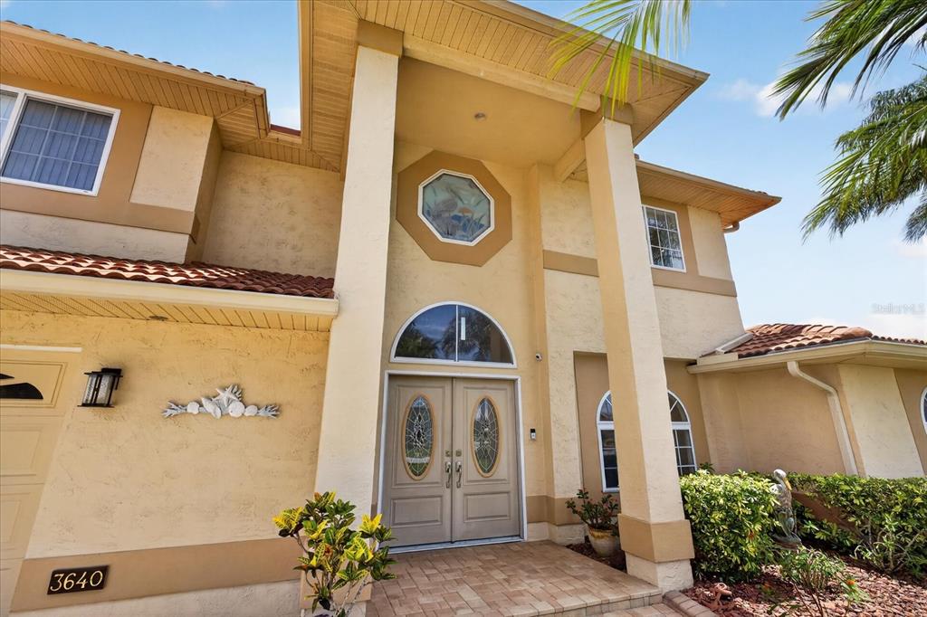 The exterior of a two-story house features a tan stucco facade, double doors, and columns — 3640 HARBORVIEW COURT, NEW PORT RICHEY, FL
