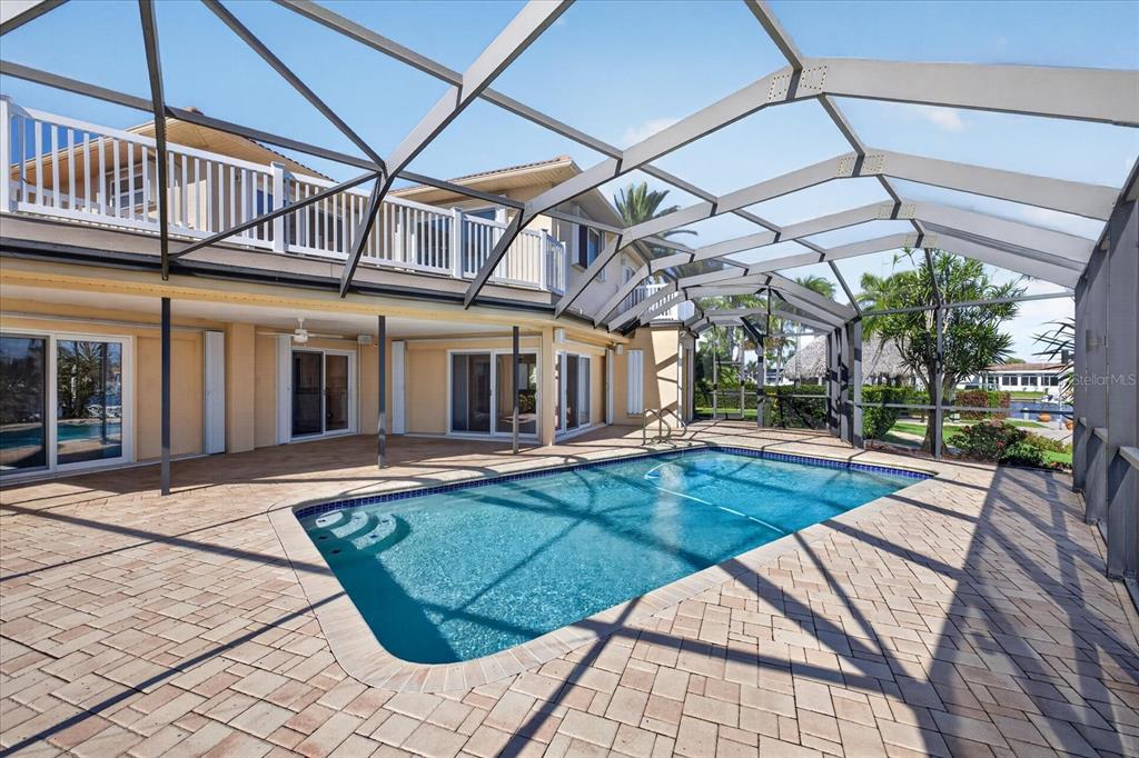 A swimming pool with a screened enclosure sits on a paved patio behind a house — 3640 HARBORVIEW COURT, NEW PORT RICHEY, FL