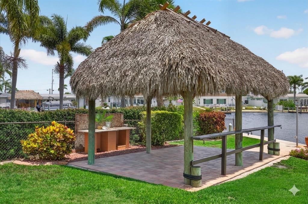 A thatched-roof tiki hut with a bar and paver patio sits beside a canal — 3640 HARBORVIEW COURT, NEW PORT RICHEY, FL