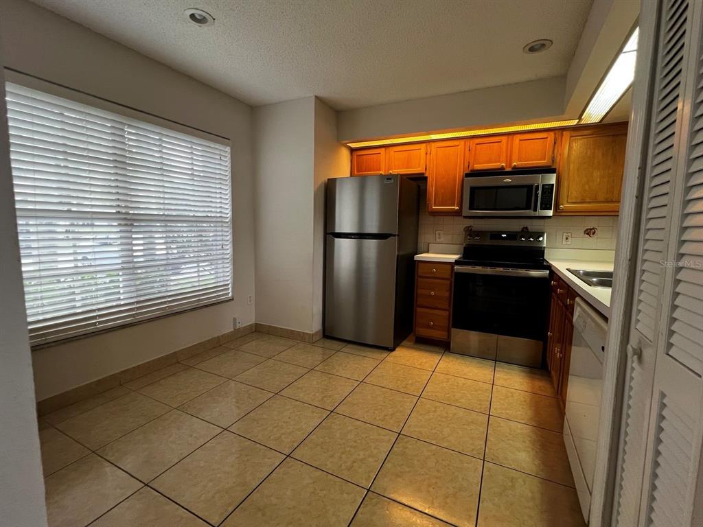 A kitchen features stainless steel appliances, wood cabinets, and light-colored tile flooring — 14426 ISLAND COVE DRIVE, ORLANDO, FL