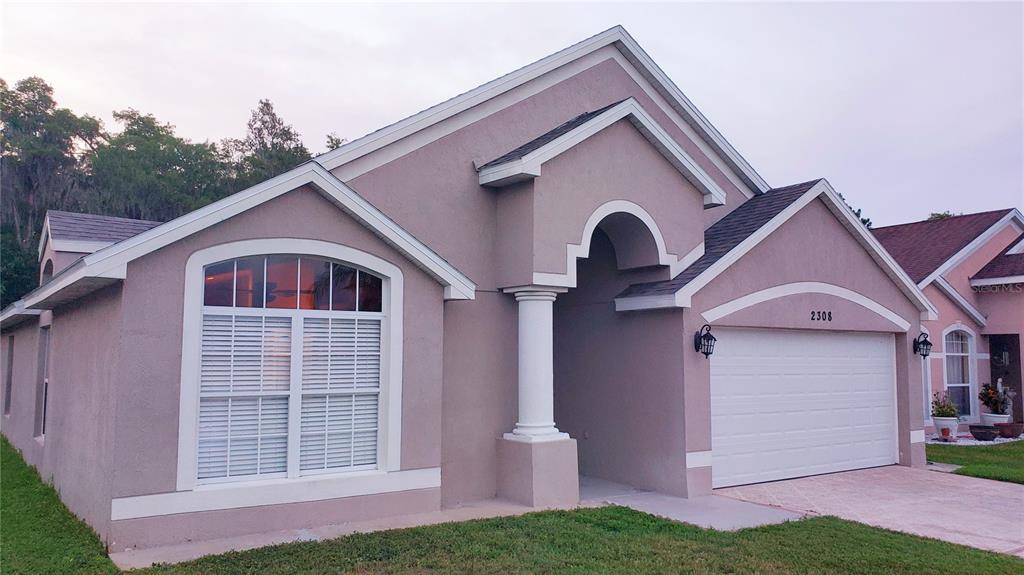A single-story house with a beige stucco exterior, a two-car garage, and a front porch — 2308 LILY PAD LANE, KISSIMMEE, FL