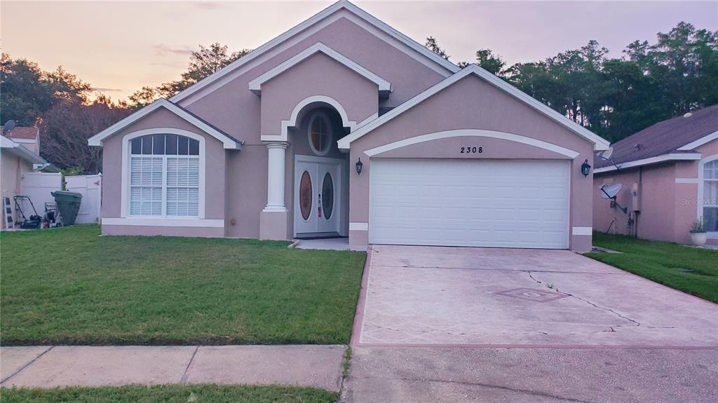 A single-story house with a tan stucco exterior, a two-car garage, and a front entryway — 2308 LILY PAD LANE, KISSIMMEE, FL