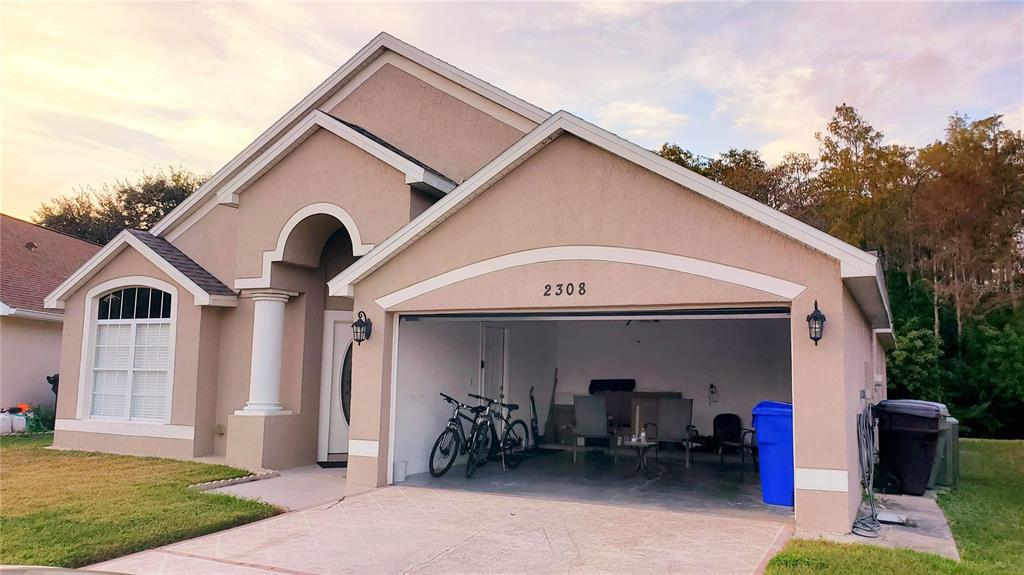 A beige single-story house features a two-car garage with two bicycles parked inside — 2308 LILY PAD LANE, KISSIMMEE, FL