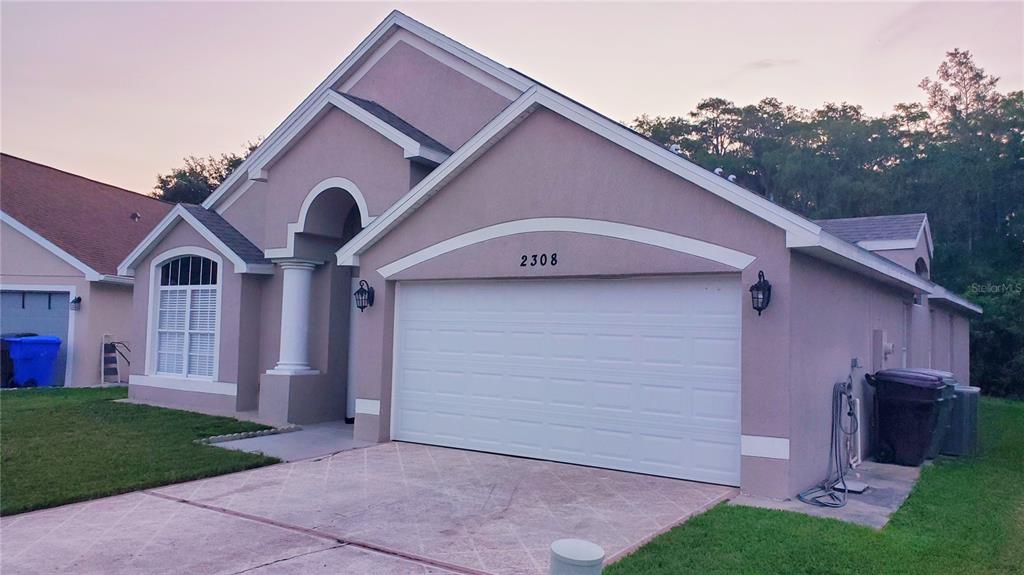 A single-story house with a beige stucco exterior, a white garage door, and a driveway — 2308 LILY PAD LANE, KISSIMMEE, FL