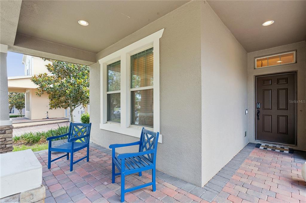 A covered front porch features brick pavers, two blue chairs, and a brown front door — 9717 WATERWAY PASSAGE DRIVE, WINTER GARDEN, FL