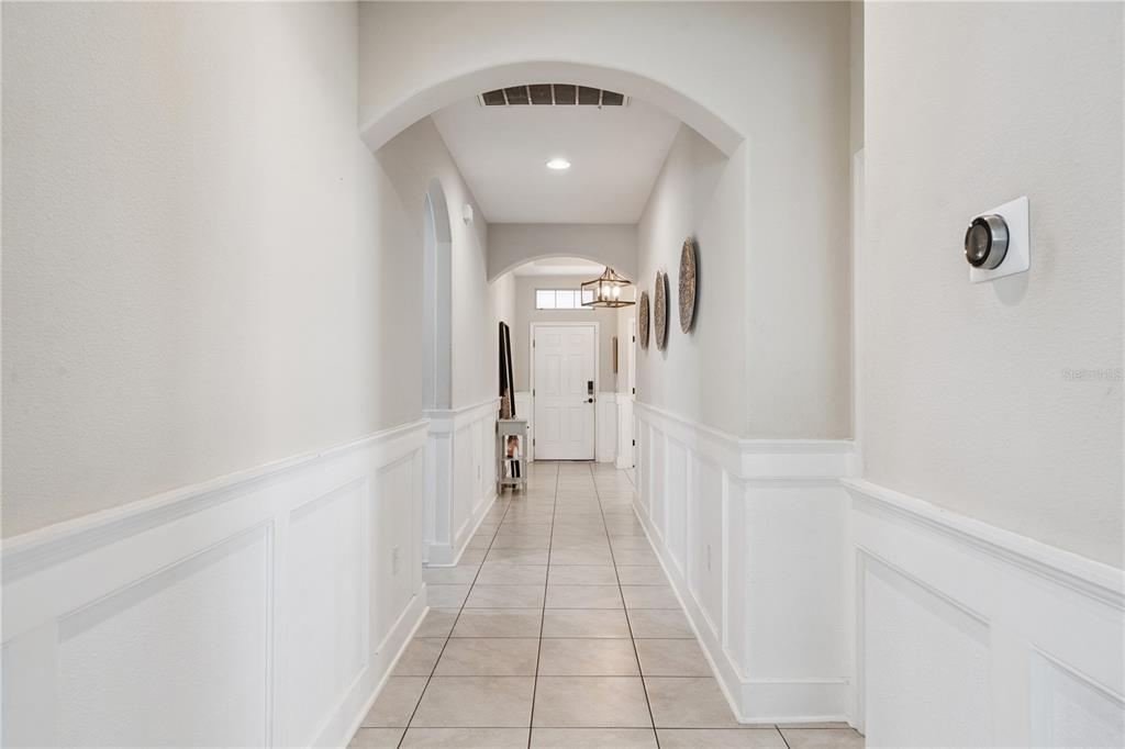 A tiled hallway features white wainscoting, arched ceilings, and a front door in the distance — 9717 WATERWAY PASSAGE DRIVE, WINTER GARDEN, FL