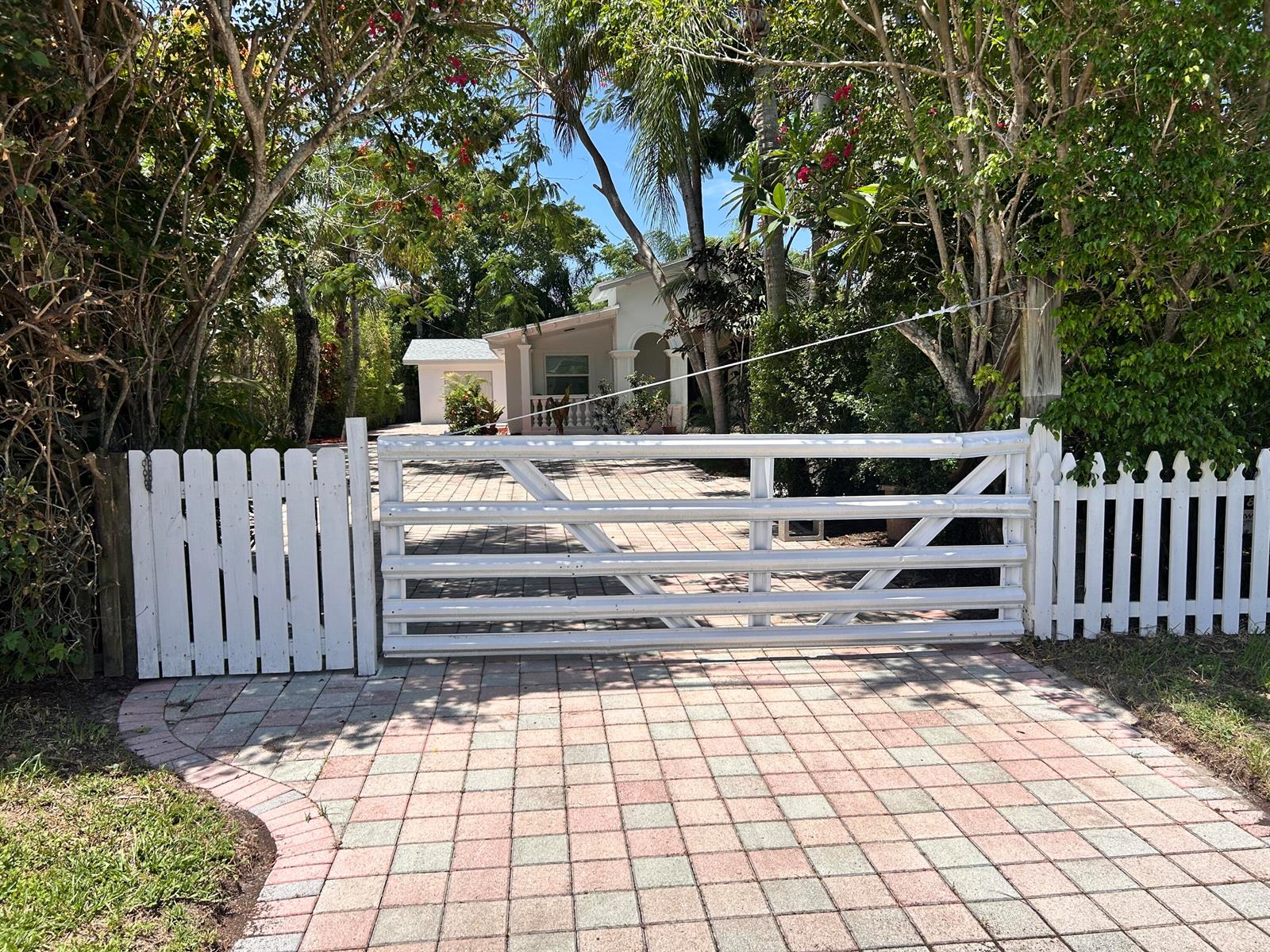 A white wooden gate blocks a paved driveway leading to a house surrounded by trees — 4793 Badger Avenue, West Palm Beach FL 33417, WEST PALM BEACH, FL