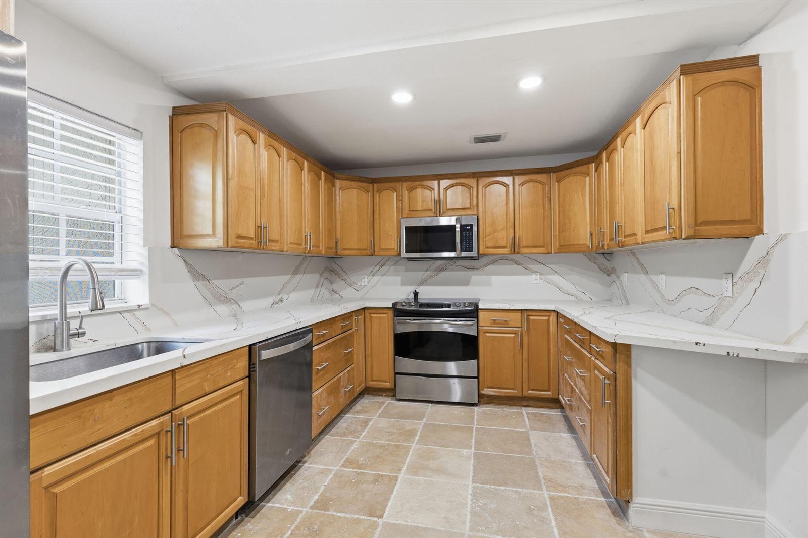 A kitchen features wood cabinets, stainless steel appliances, and white countertops with grey veining — 4793 Badger Avenue, West Palm Beach FL 33417, WEST PALM BEACH, FL