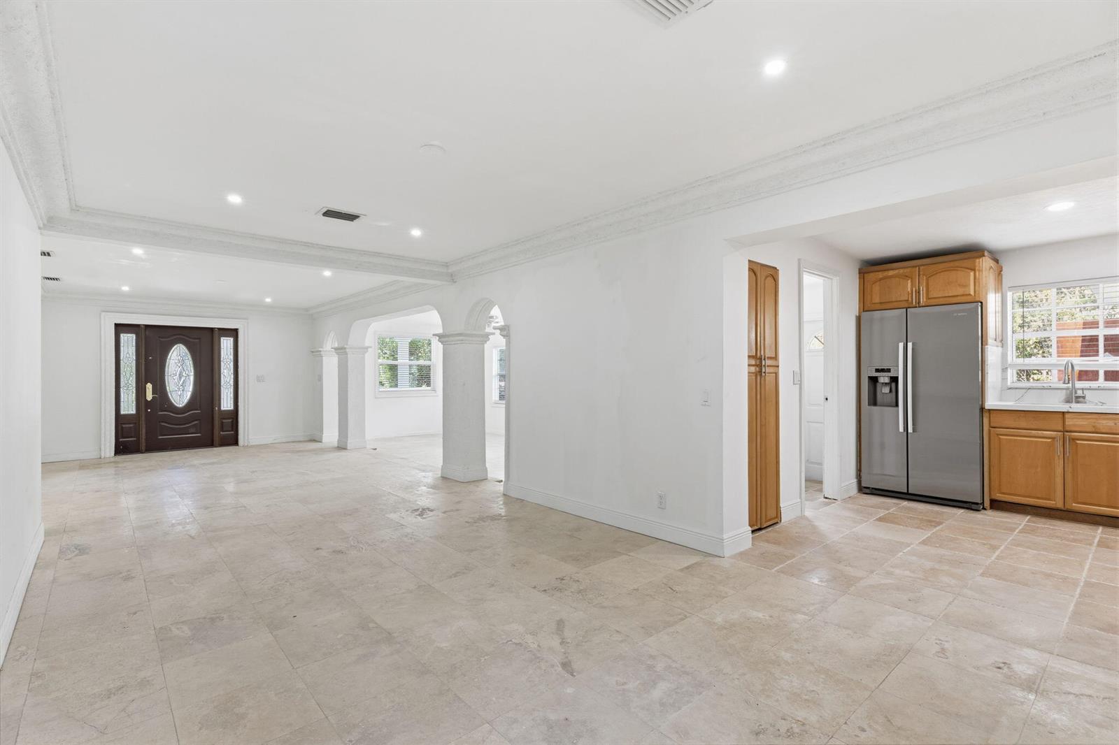 A spacious room with light tile flooring, white walls, arched columns, and a kitchen area — 4793 Badger Avenue, West Palm Beach FL 33417, WEST PALM BEACH, FL