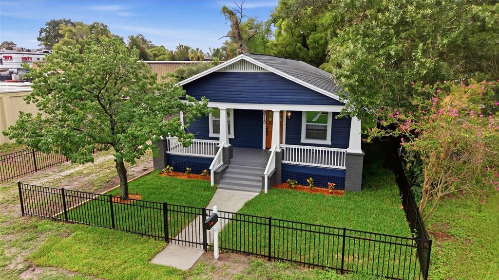 A blue bungalow with a front porch and white railings sits behind a black fence — 815 E FRIERSON AVENUE, TAMPA, FL